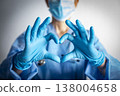 Caucasian female nurse in blue overalls and gloves showing heart shape gesture 138004658