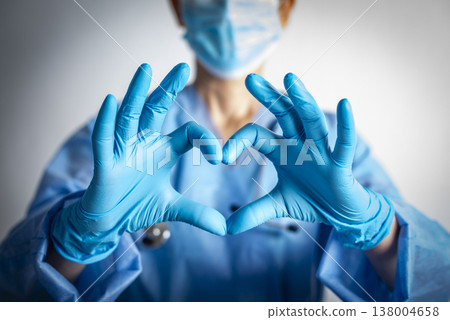 Caucasian female nurse in blue overalls and gloves showing heart shape gesture 138004658