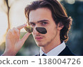 attractive man has lowered his sunglasses on his nose and is looking into the camera  138004726
