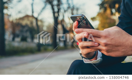Close up Male hands with smartphone, outdoors. Businessman is typing text messages on mobile phone sitting in the park. Human holds cell phone close up. Man holds mobile phone. Connection concept. 138004746