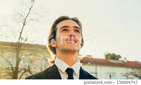 Portrait of the Handsome White man with brown hair, in the city, on the summer. Young smiling businessman looking up, outdoors. Young stylish man in business suit is on the street. People lifestyle Portrait of the Handsome White man with brown hair, in the city, on the summer. Young smiling businessman looking up, outdoors. Young stylish man in business suit is on the street. People lifestyle 138004747