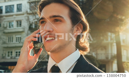 Smiling businessman in the city talking on a cell phone. Portrait Businessman in a business suit in the the street a with mobile phone. Young man in a business  suit talking on a smartphone. 138004750
