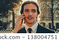 Smiling businessman in the city talking on a cell phone. Portrait Businessman in a business suit in the the street a with mobile phone. Young man in a business  suit talking on a smartphone. 138004751