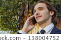 Portrait of the  Businessman in a business suit in the park  with mobile phone.  Smiling businessman talking on a cell phone., outdoors. Young man in a business  suit talking on a smartphone in nature 138004752