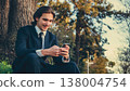 Happy man in a business suit sets outdoors and using a smartphone. Portrait of the young man in a business suit with mobile phone, in the park. Smiling businessman in city looking to a cell phone. 138004754