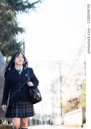 A high school girl walks along her school route in spring, smiling. A scene of students going to school as the cherry blossoms begin to bloom and the new season begins. A high school girl walks along her school route in spring, smiling. A scene of students going to school as the cherry blossoms begin to bloom and the new season begins. 138004839
