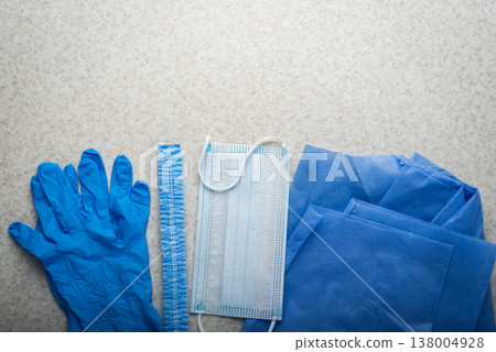 Healthcare background of disposable face mask, gloves, hat and scrubs laying on table flat lay view Healthcare background of disposable face mask, gloves, hat and scrubs laying on table flat lay view 138004928