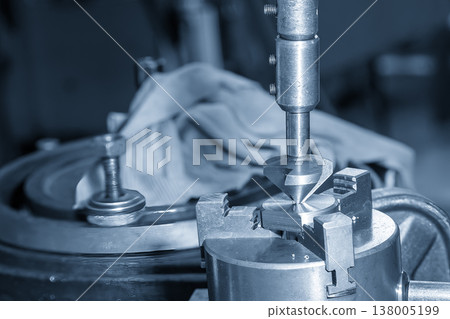 Close-up of a manual hole chamfering process on precision metal parts using a hand deburring tool in a blue-toned workshop. 138005199