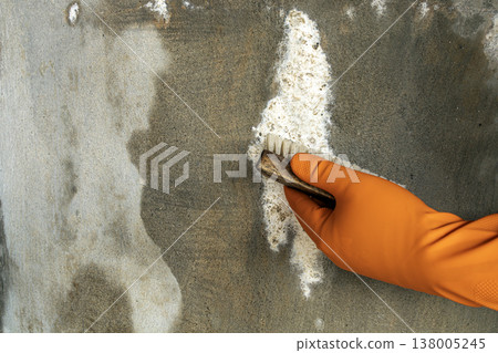 Close-Up of a Hand Wearing an Orange Protective Rubber Glove Scrubbing and Removing White Efflorescence Salt Deposits From a Damp and Stained Gray Concrete or Cement Wall Using a Stiff Bristle Brush Close-Up of a Hand Wearing an Orange Protective Rubber Glove Scrubbing and Removing White Efflorescence Salt Deposits From a Damp and Stained Gray Concrete or Cement Wall Using a Stiff Bristle Brush 138005245
