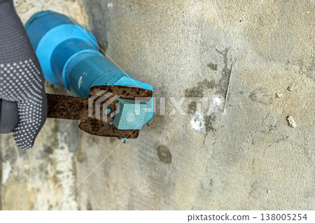 Close-Up of Construction Worker Wearing Gray Dotted Safety Gloves Using a Heavily Rusted Wrench to Tighten a Blue Hex Bolt on a Rough Concrete Wall During Building Work Close-Up of Construction Worker Wearing Gray Dotted Safety Gloves Using a Heavily Rusted Wrench to Tighten a Blue Hex Bolt on a Rough Concrete Wall During Building Work 138005254