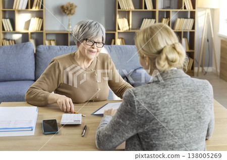 Happy senior client discussing finances with female advisor home consultation Happy senior client discussing finances with female advisor home consultation 138005269