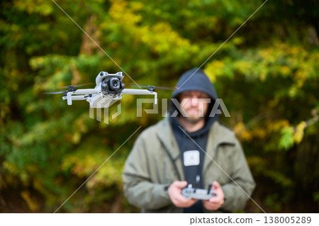 Drone flying in foreground in autumn park, quadcopter in flight with blurred man controlling it in background, aerial technology and photography concept Drone flying in foreground in autumn park, quadcopter in flight with blurred man controlling it in background, aerial technology and photography concept 138005289