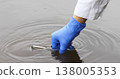 A close-up of a hand in a blue glove collecting river water with using a test tube 138005353