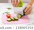 Close-up of the hands of a nine-year-old child cutting cucumber into slices with a ribbed stainless steel knife on a cutting board on a kitchen table 138005354