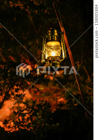 A lamp hanging in the rural, public park in the dark. Close-up of a lamp with black background. Lighting in the dark. A lamp hanging in the rural, public park in the dark. Close-up of a lamp with black background. Lighting in the dark. 138005884