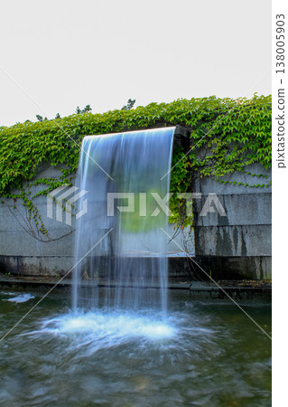 Close-up view of a cascading feature water fountain in a public park. Powerful spout of cascading water pours into the pool.  138005903
