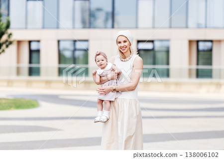 Portrait beautiful young mother with small daughter outdoors in city. Stylish woman and little girl wearing beige summer dresses, modern urban lifestyle, family love, fashion outside Portrait beautiful young mother with small daughter outdoors in city. Stylish woman and little girl wearing beige summer dresses, modern urban lifestyle, family love, fashion outside 138006102