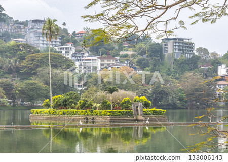 Tranquil Lake Island in a Lush Green Cityscape with Historic Architecture and Clear Reflecting Water on an Overcast Day. Kandy town in Sri Lanka. Tranquil Lake Island in a Lush Green Cityscape with Historic Architecture and Clear Reflecting Water on an Overcast Day. Kandy town in Sri Lanka. 138006143