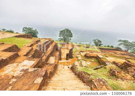Sigiriya ancient rock fortress in Sri Lanka. Ancient Staircase and Terraced Ruins Amidst Lush Greenery Under a Cloudy Sky, Reflecting Timeless Heritage and Natural Beauty 138006176