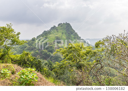 Verdant Tropical Hillside Landscape Under Overcast Sky: Lush Green Foliage and Distant Mountains Form a Serene Natural Vista. Sri Lanka island in Asia. Verdant Tropical Hillside Landscape Under Overcast Sky: Lush Green Foliage and Distant Mountains Form a Serene Natural Vista. Sri Lanka island in Asia. 138006182