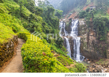 Ramboda Waterfall near Nuwara Eliya town in Sri Lanka. Footpath Alongside Lush Greenery with Majestic Waterfall Cascading Down a Rocky Cliff in a Tropical Landscape Ramboda Waterfall near Nuwara Eliya town in Sri Lanka. Footpath Alongside Lush Greenery with Majestic Waterfall Cascading Down a Rocky Cliff in a Tropical Landscape 138006187