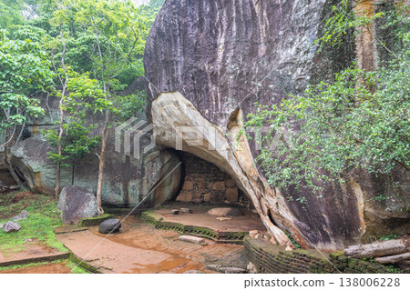 Sigiriya ancient rock fortress in Sri Lanka. Ancient cave shelter formed by massive rock formations amidst lush green jungle foliage and weathered stone paths 138006228
