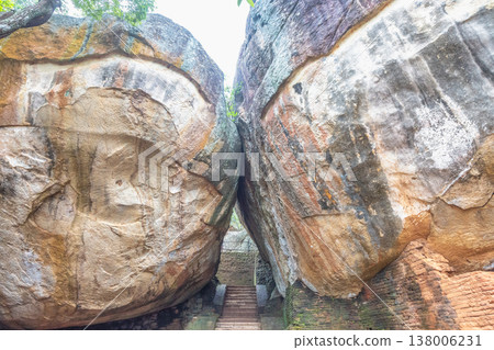 Sigiriya ancient rock fortress in Sri Lanka. Ancient Stairway Between Massive Weathered Boulders Leading Upwards, Nature's Grand Archway to Historical Wonders Sigiriya ancient rock fortress in Sri Lanka. Ancient Stairway Between Massive Weathered Boulders Leading Upwards, Nature's Grand Archway to Historical Wonders 138006231