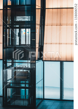 Modern glass elevator shaft with transparent structure and illuminated interior design, Contemporary lift system inside building with reflective surfaces and geometric architecture 138006552