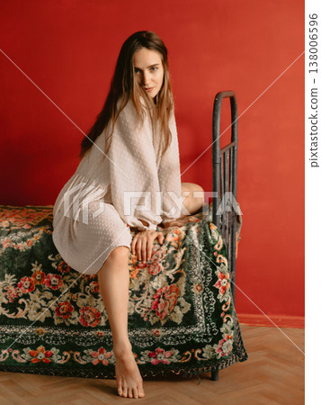 Young woman posing on vintage bed against bold red wall, artistic lifestyle portrait. Young woman posing on vintage bed against bold red wall, artistic lifestyle portrait. 138006596