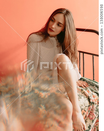 Stylish caucasian woman in boudoir dress sitting on bed with warm background and artistic light effects. Stylish caucasian woman in boudoir dress sitting on bed with warm background and artistic light effects. 138006598