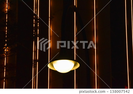 Close-up of the street light at night with buildings in the background. Cityscape and street scene at night with dark background. Close-up of the street light at night with buildings in the background. Cityscape and street scene at night with dark background. 138007542