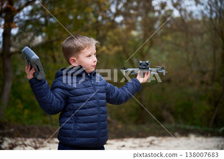 Boy flying drone in autumn park, holding quadcopter and remote controller, learning to control flight, outdoor childhood hobby and technology concept 138007683