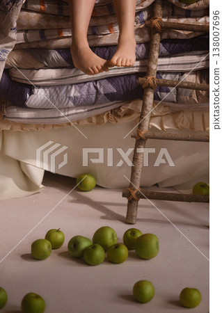 Child feet on stacked mattresses with ladder and green apples on floor, fairy tale concept 138007696
