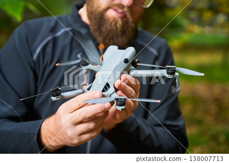Man holds drone and checks its condition before flight. Close up of hands examining quadcopter in park, inspecting body and propellers, concept of modern technology and maintenance Man holds drone and checks its condition before flight. Close up of hands examining quadcopter in park, inspecting body and propellers, concept of modern technology and maintenance 138007713