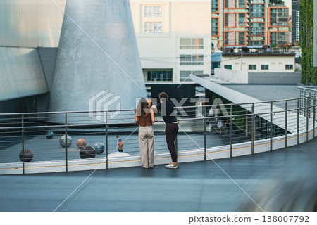 Couple standing on balcony looking at modern urban architecture in city space, Man and woman enjoying view in contemporary plaza with cityscape and contemporary Din Bangkok museum setting Couple standing on balcony looking at modern urban architecture in city space, Man and woman enjoying view in contemporary plaza with cityscape and contemporary Din Bangkok museum setting 138007792