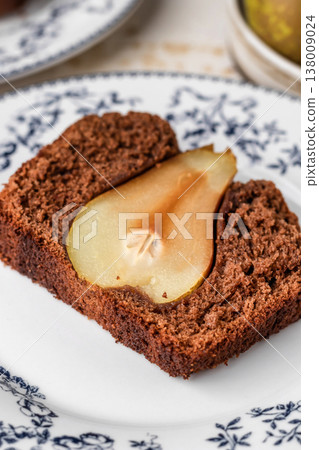 Chocolate cake with pears baked inside. Chocolate pear loaf cake with pear served on ceramic plate close up. Home cooking recipe 138009024