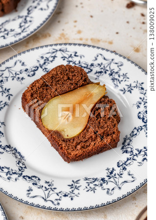 Chocolate cake with pears baked inside. Chocolate pear loaf cake with pear served on ceramic plate on beige textured background. Home cooking recipe Chocolate cake with pears baked inside. Chocolate pear loaf cake with pear served on ceramic plate on beige textured background. Home cooking recipe 138009025