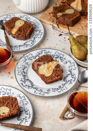 Chocolate cake with pears baked inside. Chocolate pear loaf cake with pear served on ceramic plates and tea on beige textured background. Home cooking recipe 138009026