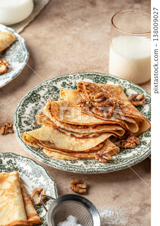 Delicious crepes served with nuts folded on ceramic plate. Tasty morning breakfast on beige table background, Maslenitsa concept Delicious crepes served with nuts folded on ceramic plate. Tasty morning breakfast on beige table background, Maslenitsa concept 138009027