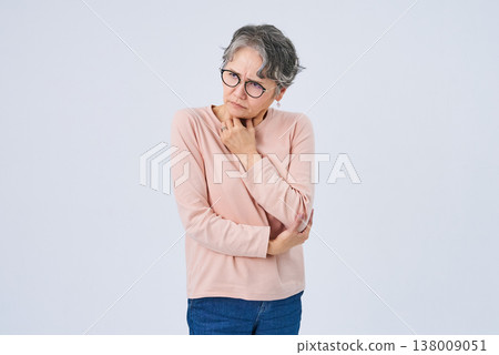 A senior woman appears to be experiencing discomfort in her throat. 138009051