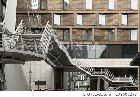 Unspooling like a metallic ribbon, the silver staircase of the Millennium Bridge cuts a dynamic path through the air, its airy, kinetic form standing in stark relief against a solid, bronze-hued Unspooling like a metallic ribbon, the silver staircase of the Millennium Bridge cuts a dynamic path through the air, its airy, kinetic form standing in stark relief against a solid, bronze-hued 138009258