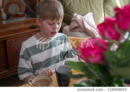 Boy sits at table with drink and toy in home interior with natural light and flowers in foreground, everyday moment of focus and activity. Childhood activity, family life, lifestyle, home environment Boy sits at table with drink and toy in home interior with natural light and flowers in foreground, everyday moment of focus and activity. Childhood activity, family life, lifestyle, home environment 138009643