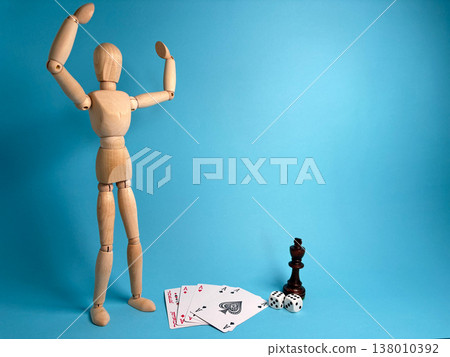 Wooden figure stands with raised arms near playing cards and a chess piece on a blue background Wooden figure stands with raised arms near playing cards and a chess piece on a blue background 138010392