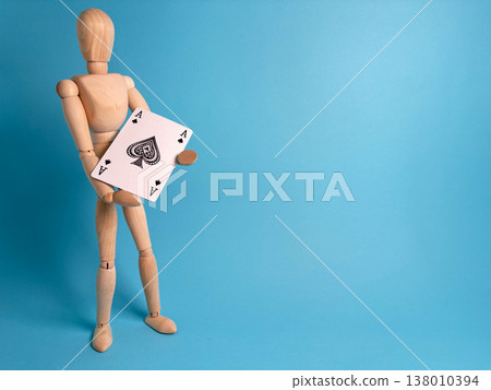 Wooden figure holds playing card showing two aces against blue background while standing in studio Wooden figure holds playing card showing two aces against blue background while standing in studio 138010394