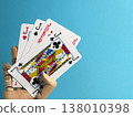 Playing cards held by a wooden hand on a blue background with different card ranks shown and joker present in the hand 138010398