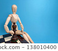 Wooden figure sits on a chessboard with a king piece in front against a blue background showing a game in progress 138010400