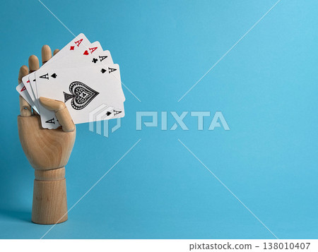 Playing cards held by a wooden hand against a blue background with focus on four aces and a heart symbol 138010407
