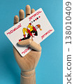 Hand holds playing card with jester design against blue background while showing creative display 138010409