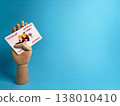 Holding a playing card with a wooden hand against a blue background in a studio setting during daylight 138010410