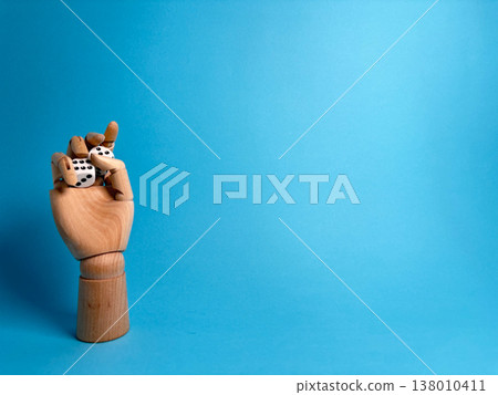 Wooden hand holds two dice against a bright blue background in a playful display of chance and games 138010411